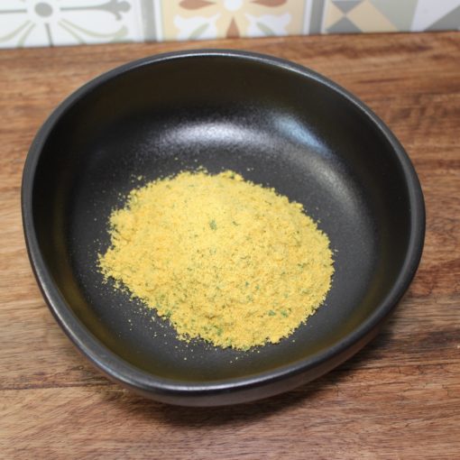 Poudre jaune dans un bol noir sur une table en bois, devant un fond en carreaux colorés.