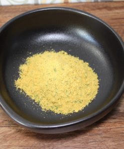 Poudre aromatique jaune dans un bol noir sur une table en bois, idéale pour assaisonner vos plats.