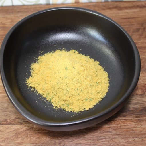 Poudre aromatique jaune dans un bol noir sur une table en bois, idéale pour assaisonner vos plats.