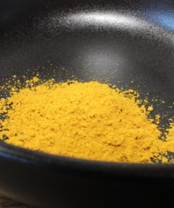 Poudre jaune épicée dans un bol noir, idéale pour agrémenter vos plats de saveurs exotiques et colorées.