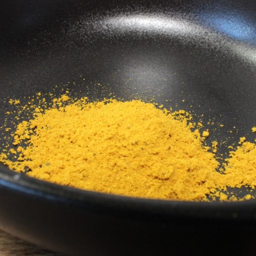 Poudre jaune épicée dans un bol noir, idéale pour agrémenter vos plats de saveurs exotiques et colorées.