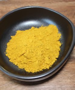 Poudre de curry jaune vif dans un bol noir sur une table en bois, parfaite pour épicer vos plats.