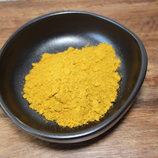 Poudre de curry jaune vif dans un bol noir sur une table en bois, parfaite pour épicer vos plats.