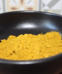 Poudre de curry jaune dans un bol noir sur table en bois, avec carrelage en arrière-plan.
