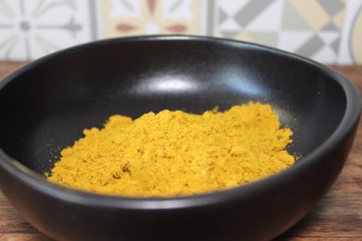 Poudre de curry jaune dans un bol noir sur table en bois, avec carrelage en arrière-plan.