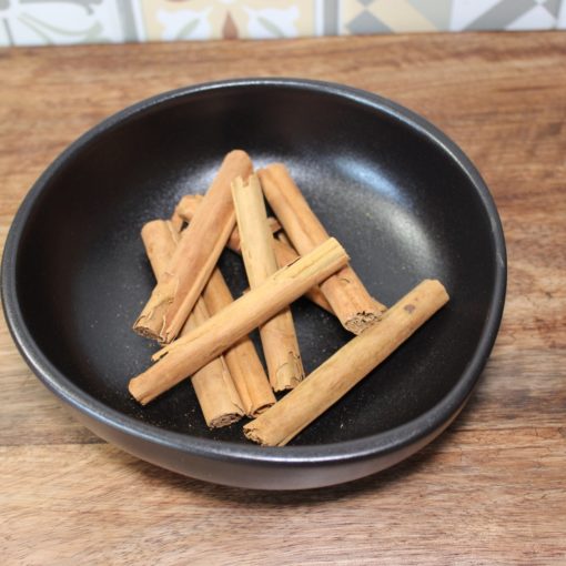 Bâtons de cannelle dans un bol noir sur une table en bois, idéal pour la cuisine et les recettes sucrées et épicées.
