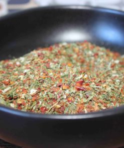 Mélange coloré d'herbes et épices dans un bol noir, idéal pour assaisonner vos plats avec goût et arômes.