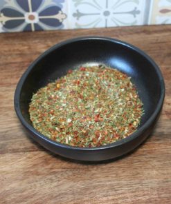 Assortiment coloré d'herbes et d'épices dans un bol noir sur une table en bois, fond de carreaux décoratifs.