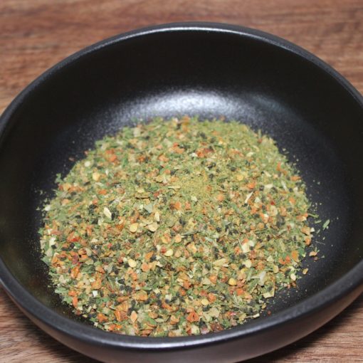 Mélange d'épices séchées dans un bol noir sur une table en bois, prêt pour la cuisine.