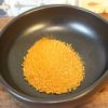 Granules d'oignon séché dans un bol noir sur fond de carreaux colorés.