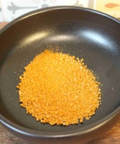 Granules d'oignon séché dans un bol noir sur fond de carreaux colorés.