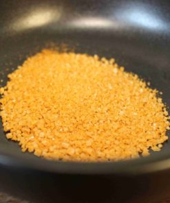 Poudre jaune dans un bol noir, utilisée en cuisine pour ajouter du goût et de la texture aux plats.