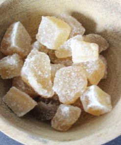 Morceaux de gingembre confit dans un bol en bois, parfaits pour une touche sucrée et épicée dans vos recettes.