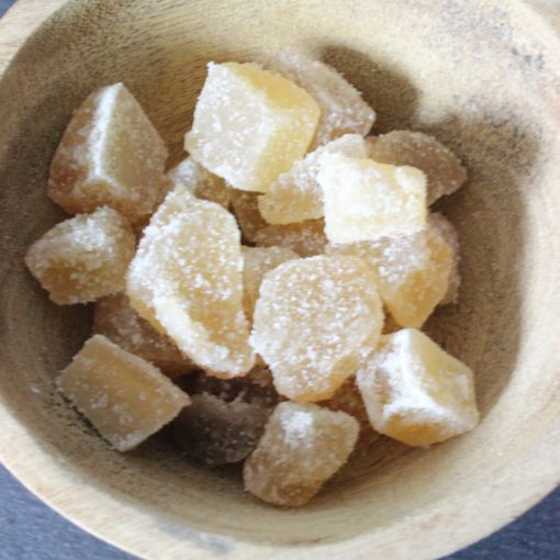Morceaux de gingembre confit dans un bol en bois, parfaits pour une touche sucrée et épicée dans vos recettes.