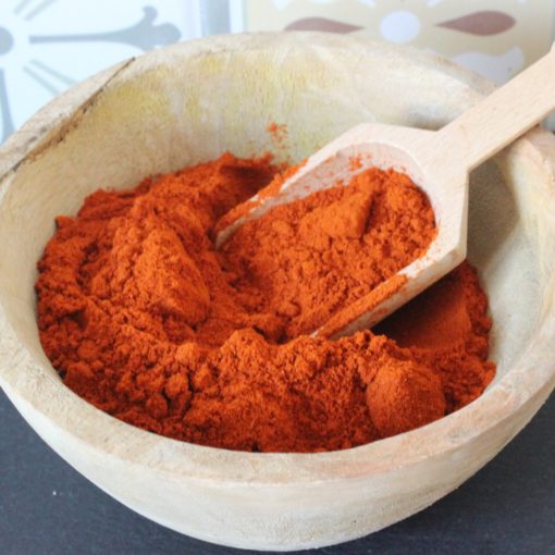 Bol en bois rempli de paprika rouge en poudre avec une cuillère en bois, sur fond de motif coloré.