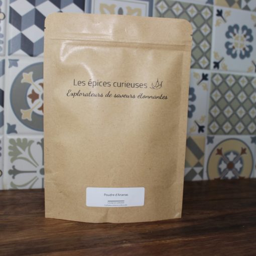 Sachet de poudre d'ananas des Épices Curieuses, fond carrelage coloré, saveurs étonnantes à explorer.