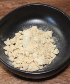 Poudre alimentaire jaune dans un bol noir sur une table en bois, vue rapprochée.