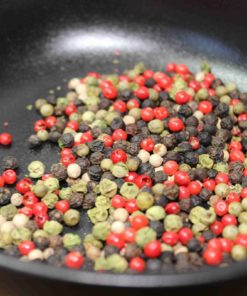 Mélange coloré de grains de poivre dans une poêle, idéal pour rehausser les plats avec une touche épicée et aromatique.