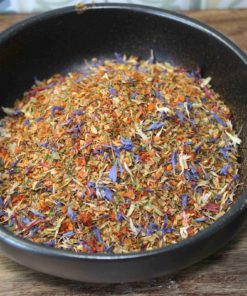 Mélange coloré d'épices séchées dans un bol noir sur une table en bois, idéal pour relever vos plats.