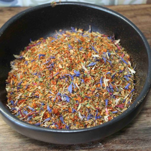 Mélange coloré d'épices séchées dans un bol noir sur une table en bois, idéal pour relever vos plats.