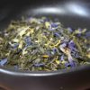 Mélange de thé vert avec fleurs séchées dans un bol noir. Arômes naturels et couleurs vives pour une infusion délicate.