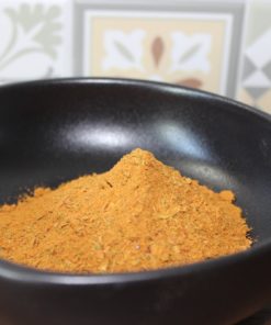 Bol noir rempli de poudre jaune épicée, fond de carreaux géométriques et floraux en cuisine.