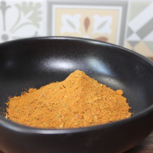 Bol noir rempli de poudre jaune épicée, fond de carreaux géométriques et floraux en cuisine.