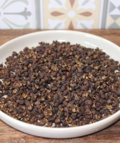 Grains de poivre de Sichuan dans une assiette blanche sur une table en bois, fond de motifs colorés.