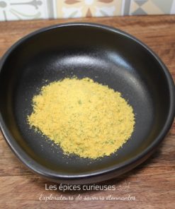 Poudre jaune dans un bol noir sur une table en bois, devant un fond en carreaux colorés.