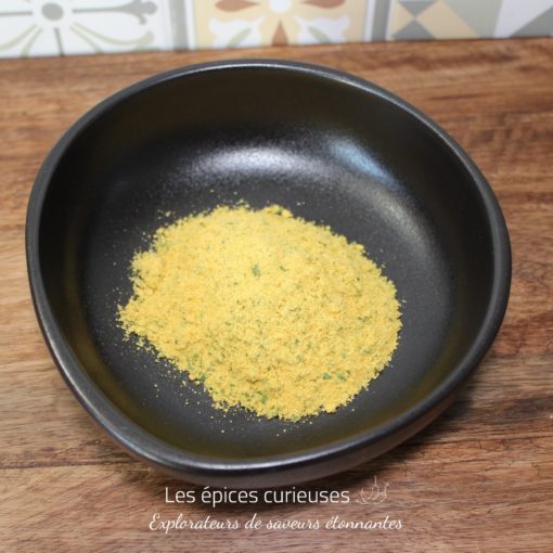Poudre jaune dans un bol noir sur une table en bois, devant un fond en carreaux colorés.