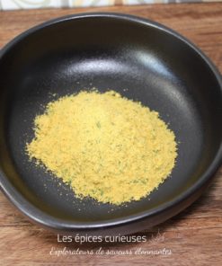 Poudre aromatique jaune dans un bol noir sur une table en bois, idéale pour assaisonner vos plats.