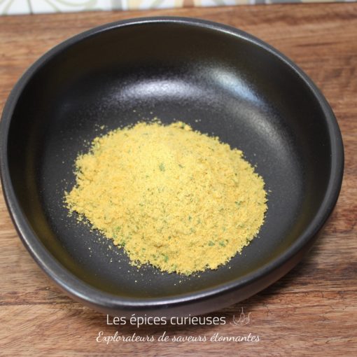 Poudre aromatique jaune dans un bol noir sur une table en bois, idéale pour assaisonner vos plats.