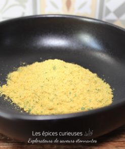 Assaisonnement en poudre jaune dans un bol noir sur fond de carreaux, parfait pour relever vos plats.