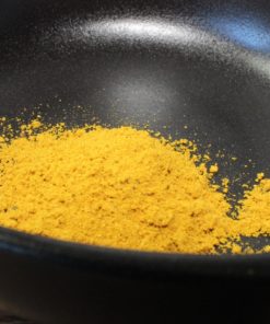 Poudre de curry jaune vif dans un bol noir, ajout exotique idéal pour rehausser vos plats avec une saveur épicée.