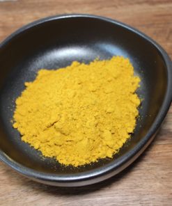 Poudre de curry jaune vif dans un bol noir sur une table en bois, parfaite pour épicer vos plats.
