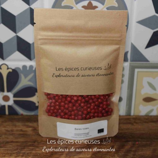 Sachet de baies roses Les épices curieuses sur table en bois, fond de carrelage coloré.
