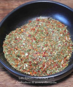 Assaisonnement aux herbes et épices dans un bol noir sur une table en bois.