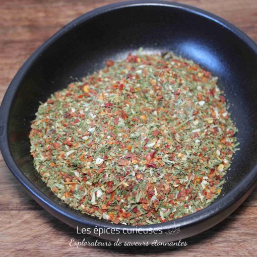 Assaisonnement aux herbes et épices dans un bol noir sur une table en bois.