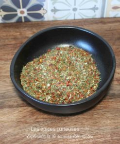 Assortiment coloré d'herbes et d'épices dans un bol noir sur une table en bois, fond de carreaux décoratifs.