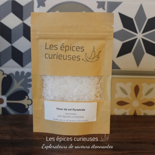 Fleur de sel Pyramide par Les Épices Curieuses, sur fond de carreaux géométriques. Gourmet et esthétique.