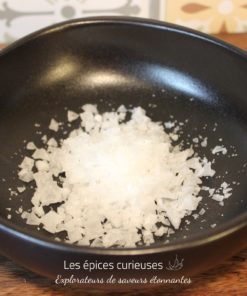 Flocons de sel de mer dans un bol noir, parfaits pour relever vos plats gourmet.