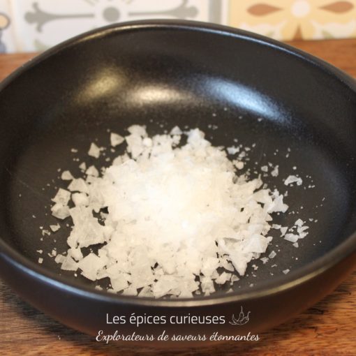 Flocons de sel de mer dans un bol noir, parfaits pour relever vos plats gourmet.