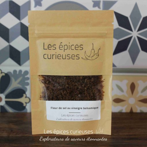 Fleur de sel au vinaigre balsamique Les épices curieuses devant un fond géométrique coloré.