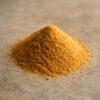 Tas de poudre jaune-orange sur surface grise, évoquant épices culinaires, ingrédients biologiques ou poudres alimentaires.