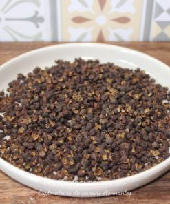 Grains de poivre de Sichuan dans une assiette blanche sur une table en bois, fond de motifs colorés.