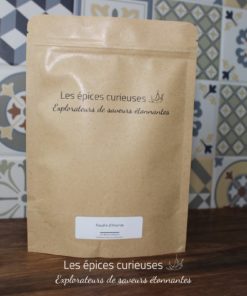 Sachet de poudre d'ananas des Épices Curieuses, fond carrelage coloré, saveurs étonnantes à explorer.