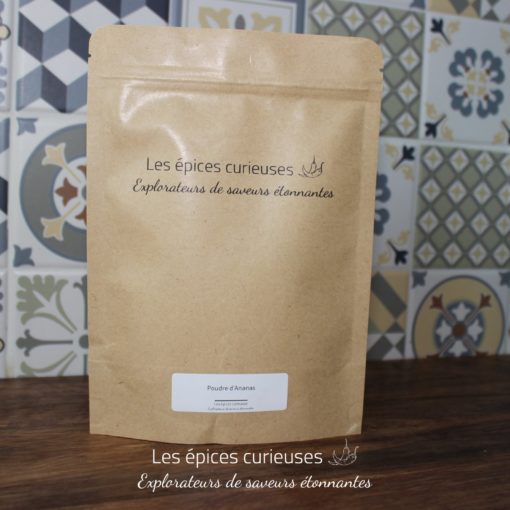 Sachet de poudre d'ananas des Épices Curieuses, fond carrelage coloré, saveurs étonnantes à explorer.