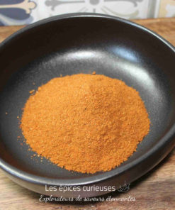 Poudre de piment doux dans un bol noir sur une table en bois, prêt pour des recettes savoureuses.