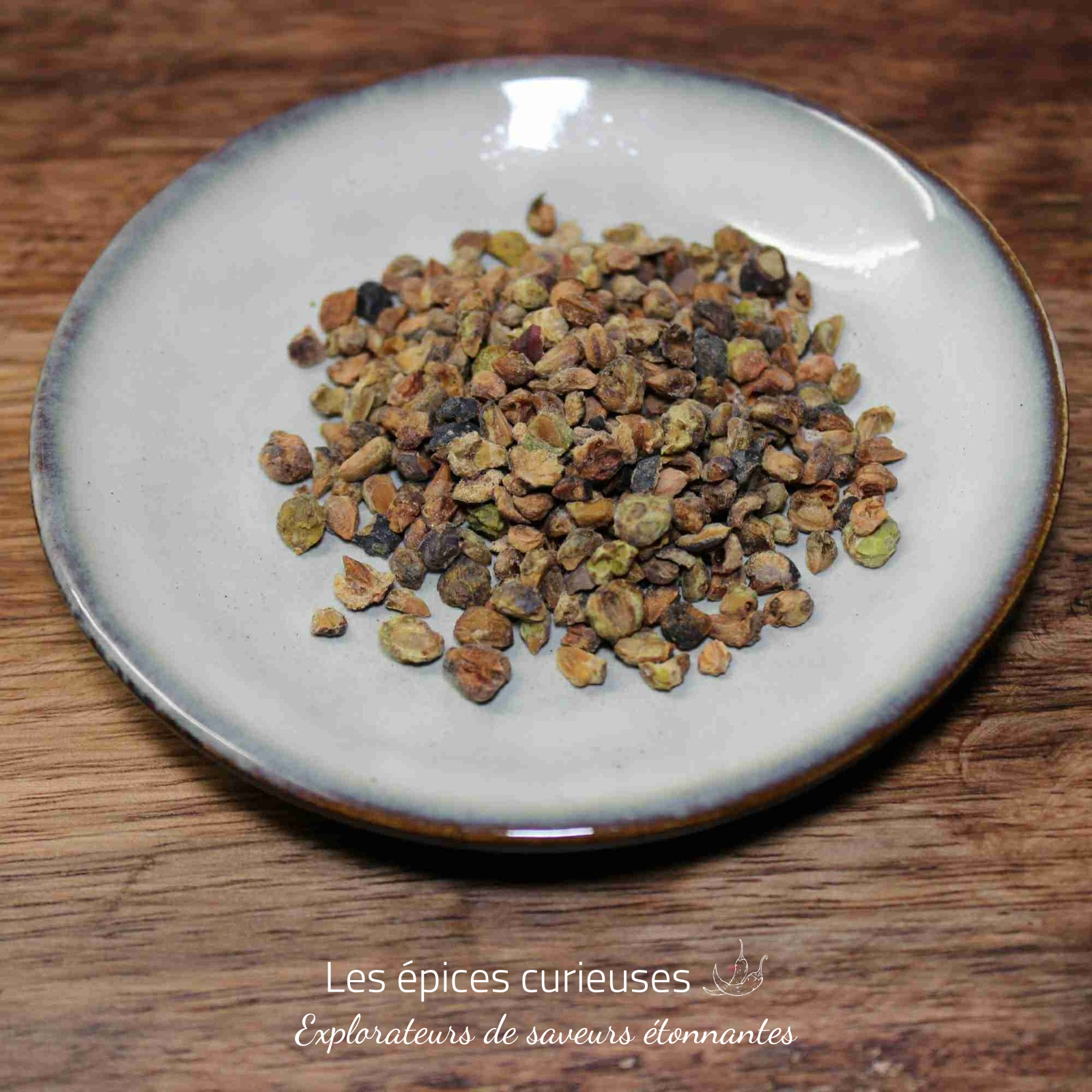 Baies de genievre concassé (3) Assiette de graines de cardamome séchées sur une table en bois, vue rapprochée pour un usage culinaire ou aromatique.