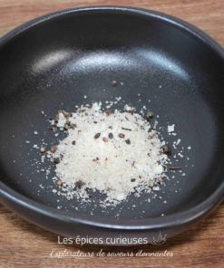 Sel épicé dans un bol noir sur une table en bois, prêt à assaisonner des plats.